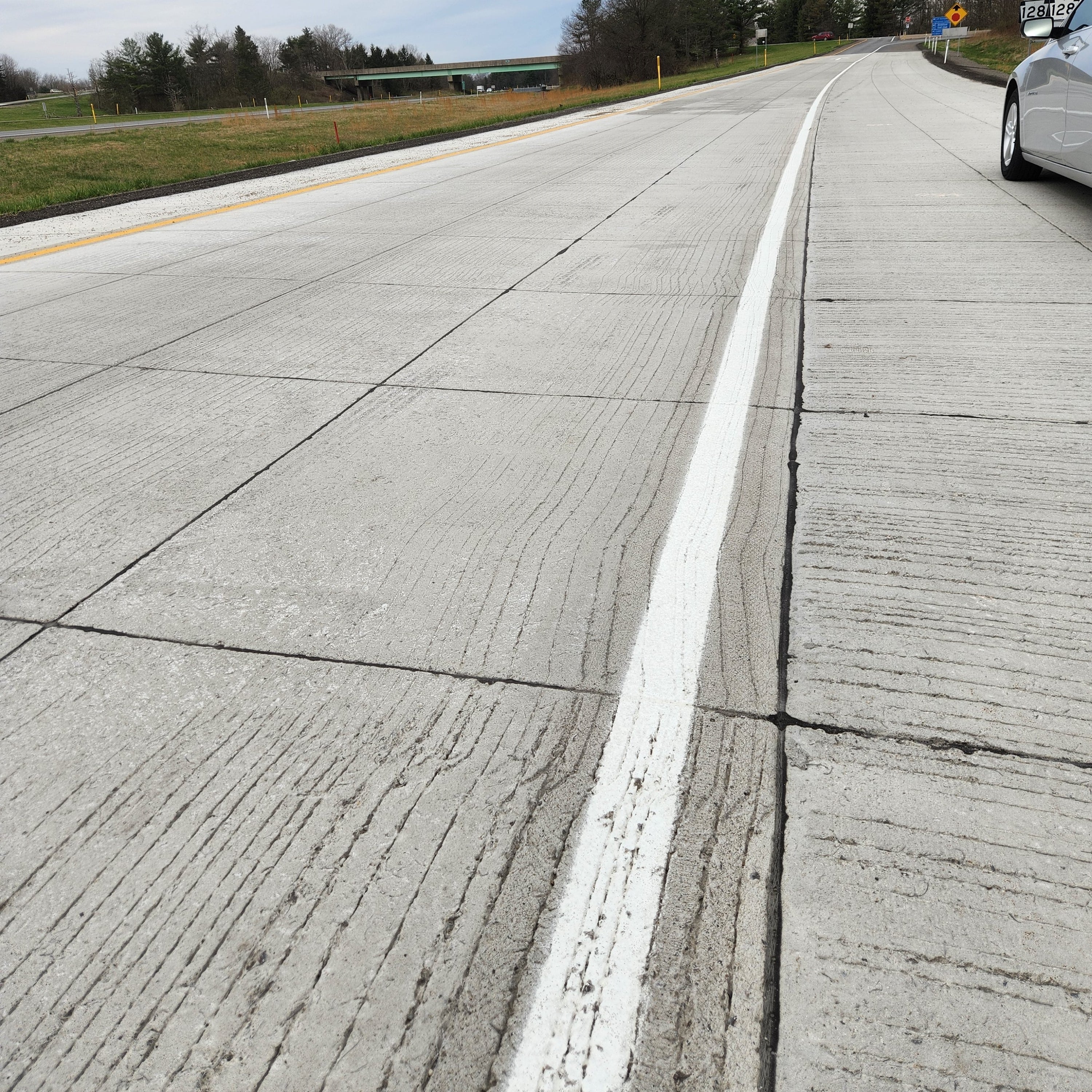 An image showing a close up look of the thin-bonded concrete overlay placement on an exit ramp with a silver car parked on the shoulder of the ramp 
